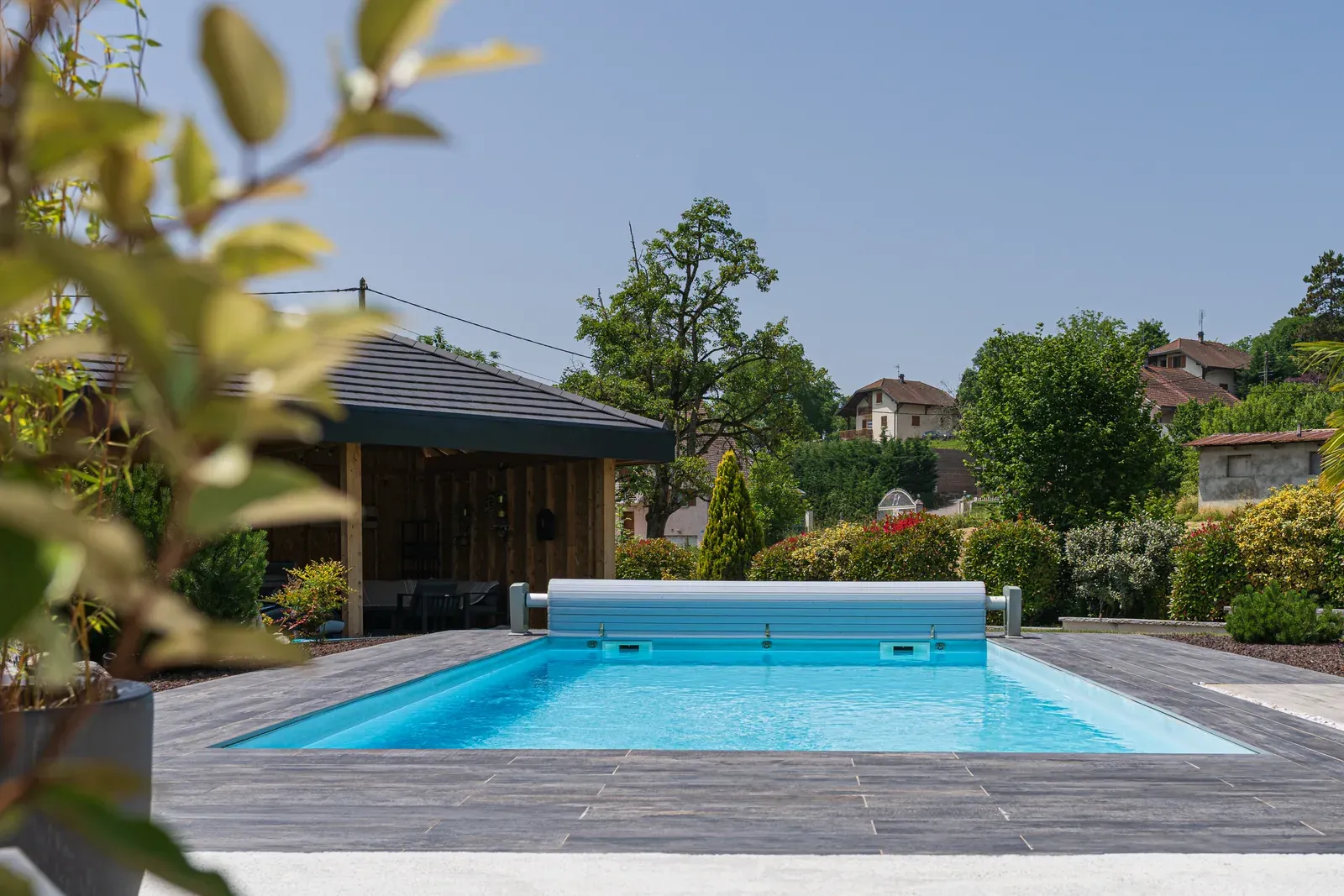 Piscine rectangulaire à volet immergé, margelles en pierre et pool house en bois, à Viuz-en-Sallaz