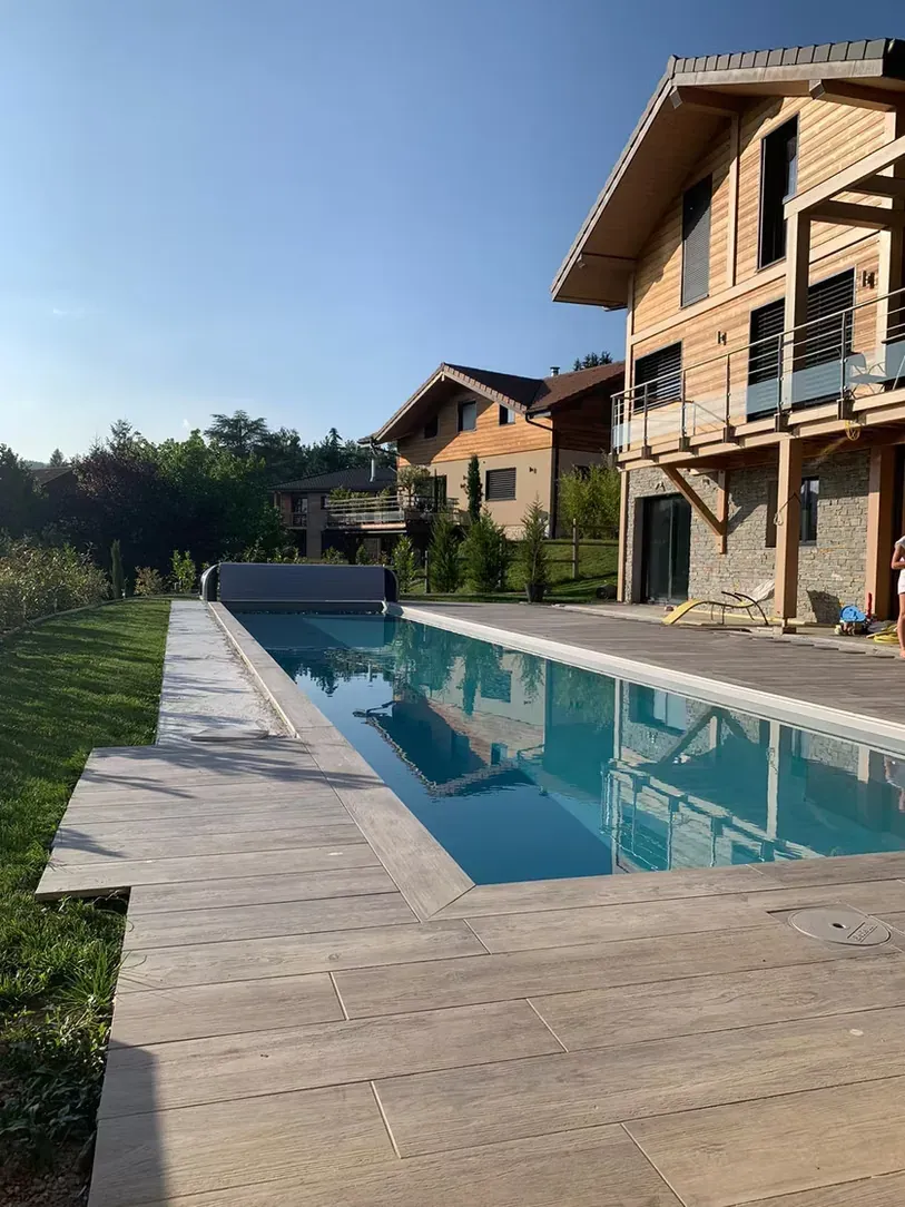Couloir de nage bordé d’une terrasse en lames de bois, devant un chalet contemporain en bois et pierre