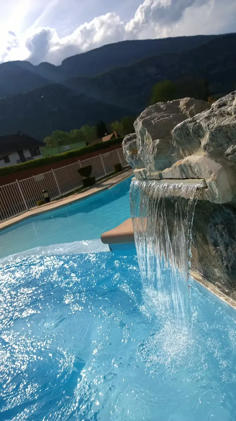 Cascade sur enrochement se déversant dans une piscine collective, massif montagneux en arrière-plan