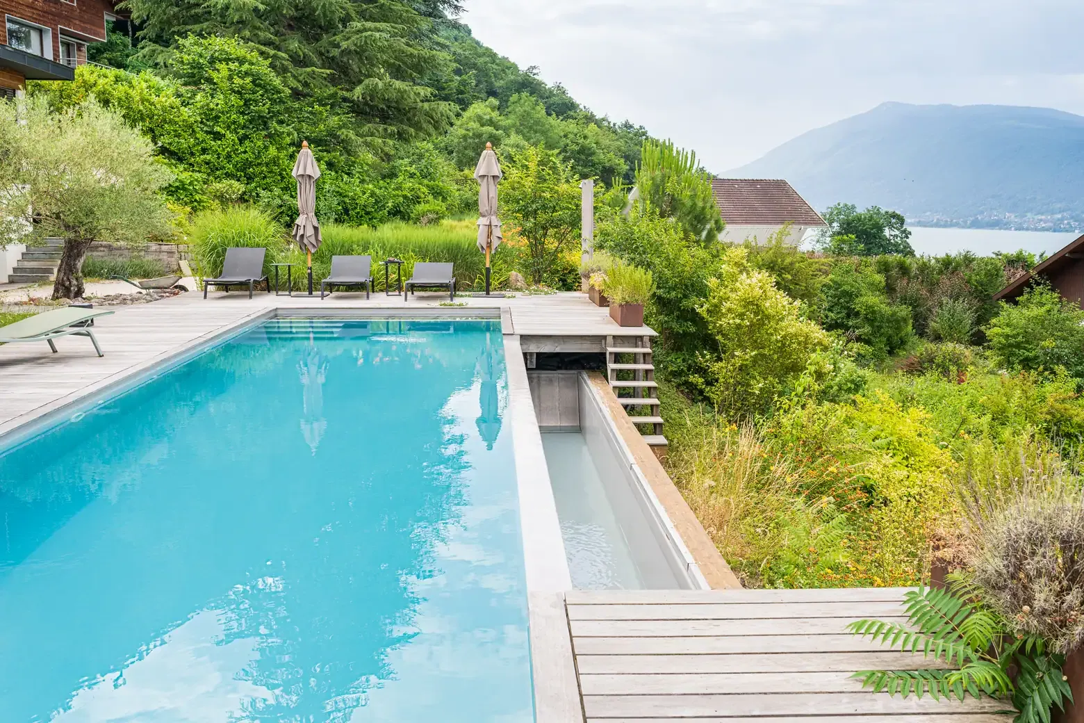 Piscine avec escalier immergé et terrasse bois dans un jardin arboré à Annecy-le-Vieux
