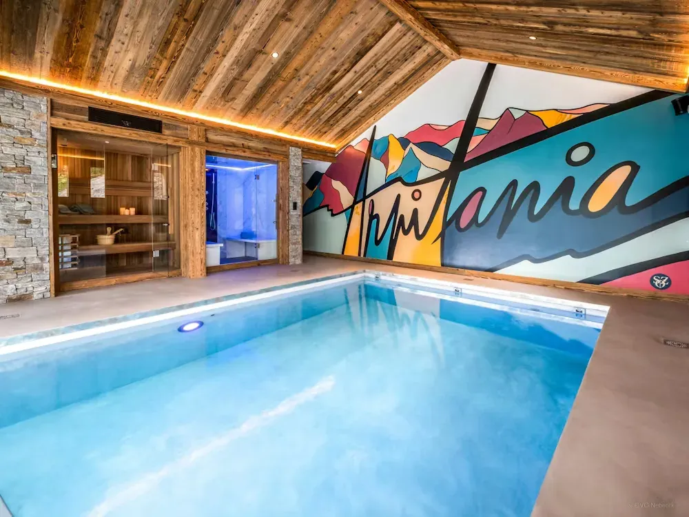 Piscine intérieure d’un chalet avec sauna et hammam attenants, sous une charpente en vieux bois