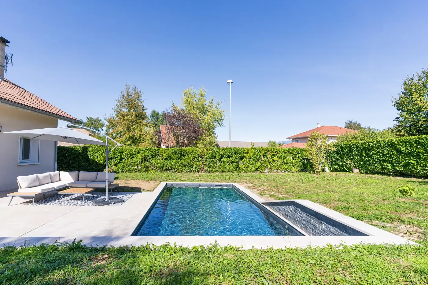 Piscine avec transats et parasol dans un jardin clos par une haie à Annecy