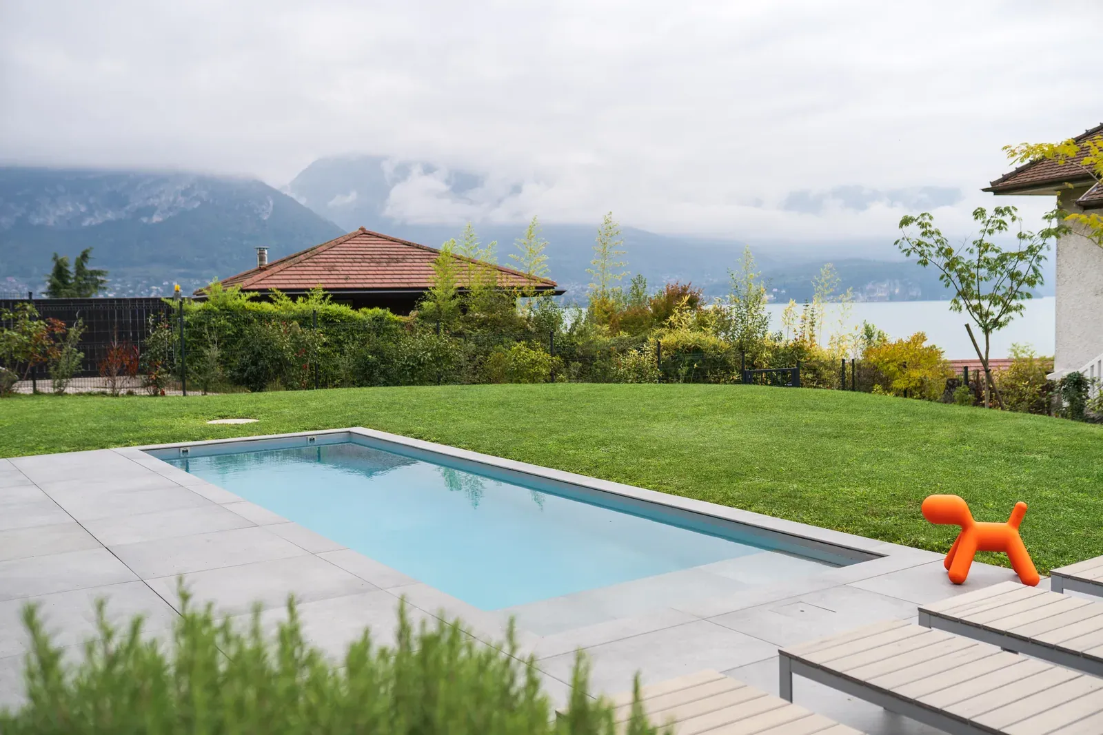 Grande piscine rectangulaire bordée d’une pelouse et de collines boisées à Sévrier