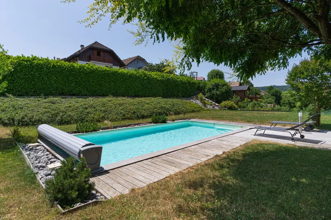 Piscine avec volet roulant immergé et terrasse en bois dans un jardin à Poisy